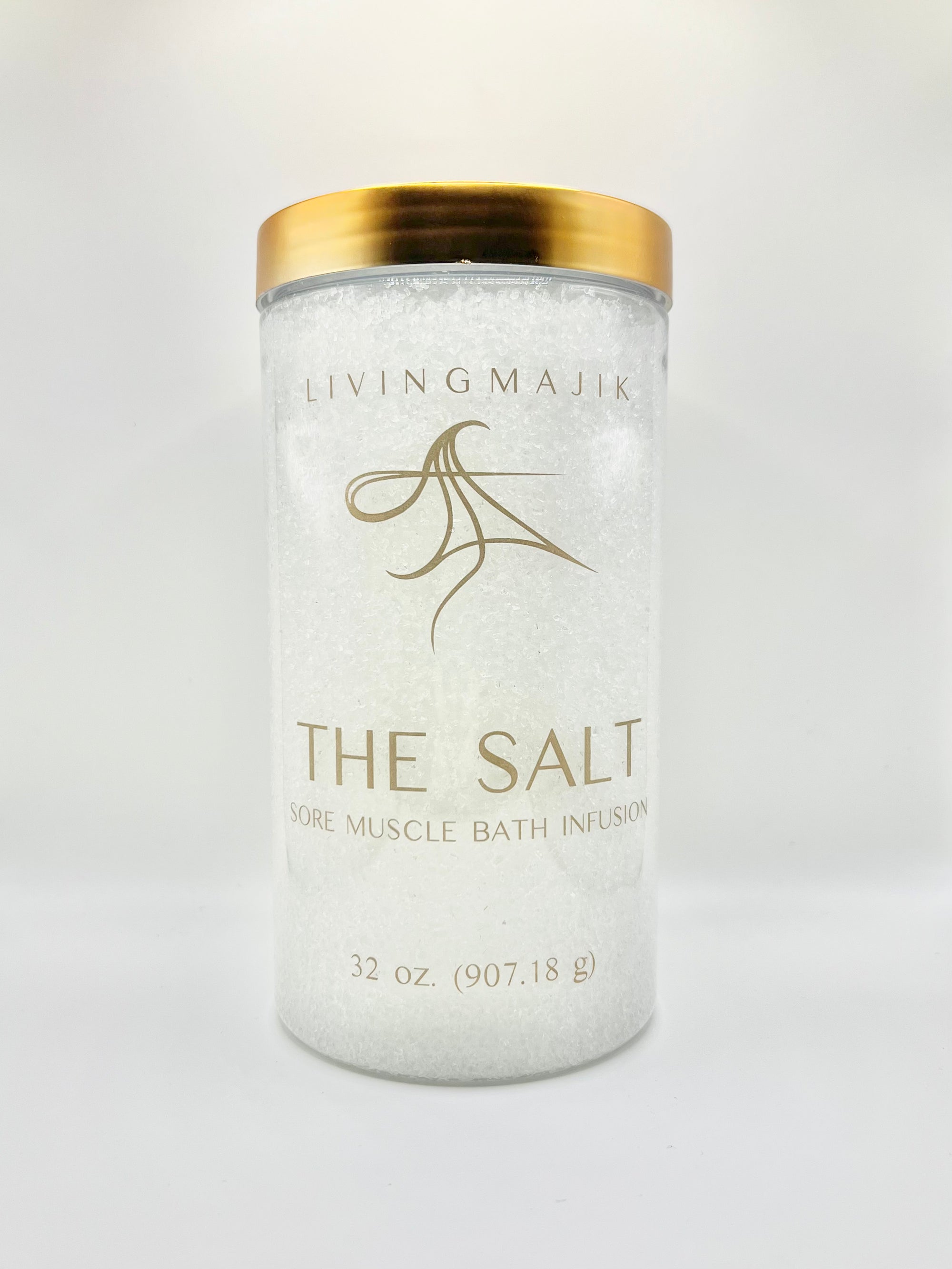 Picture of Livingmajik's Sore Muscle Bath Infusion THE SALT in a clear bath safe container with gold writing and a gold lid. Sophisticated addition to an elegant bathroom for luxurious baths to relief muscle discomfort and achieve relaxation.