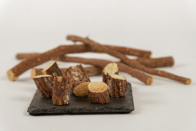 A close-up image of dried licorice root sticks, showcasing their rough, fibrous texture and natural brown color, arranged on a black slate surface.
